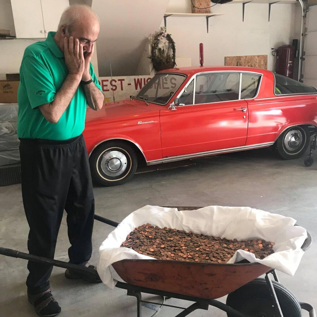 Joe Iafrancesco in his garage with a wheelbarrow full of pennies with a red classic car in the background